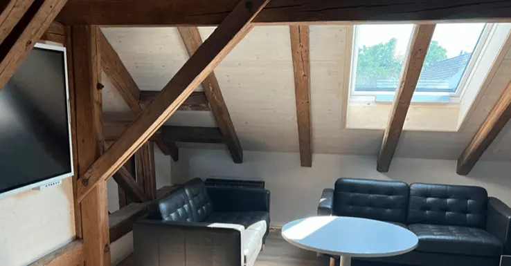 Showroom Ottikon: Dachgeschoss mit Holzbalken, grossem Bildschirm, Sofas und Rundtisch